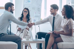 a group of people sitting around a table shaking hands.