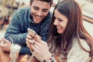 a man and woman sitting at a table looking at a cell phone.